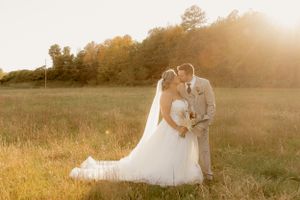 Wedding couple embracing in golden sunlit field during sunset.