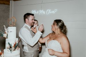 A joyful wedding cake cutting moment at a rustic venue with neon signage.
