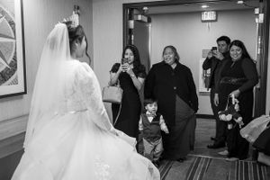 A wedding scene with guests watching and taking photos in a hallway.