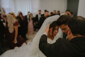 An intimate wedding moment captured during a reception with guests in the background.