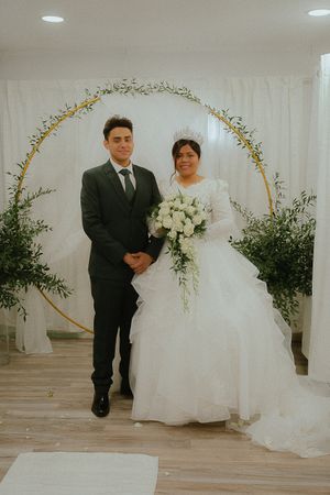 A wedding portrait under a floral arch with white drapery and greenery.