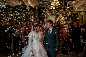 Newlyweds celebrating under a shower of white petals with string lights overhead.
