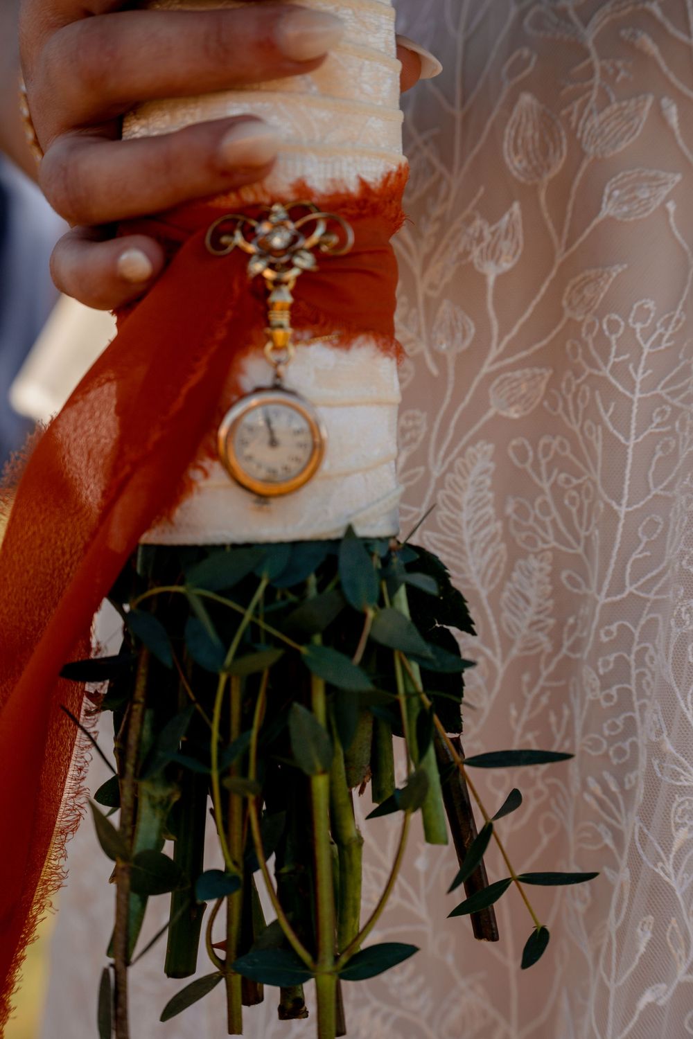 Vintage pocket watch with ornate details hanging against a floral patterned background.