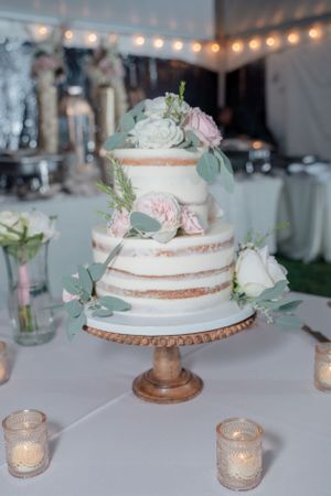 Semi-naked wedding cake decorated with fresh flowers and eucalyptus on a wooden cake stand.