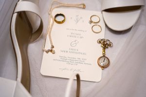 Wedding invitation with rings and vintage pocket watch arranged on white fabric.