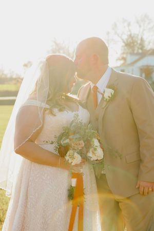 Romantic sunset portrait of newlyweds sharing an intimate moment with bouquet.
