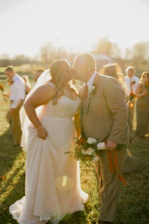 Newlyweds share a tender moment in golden sunlight surrounded by wedding party.