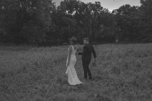 Black and white photo of couple walking through field on wedding day.