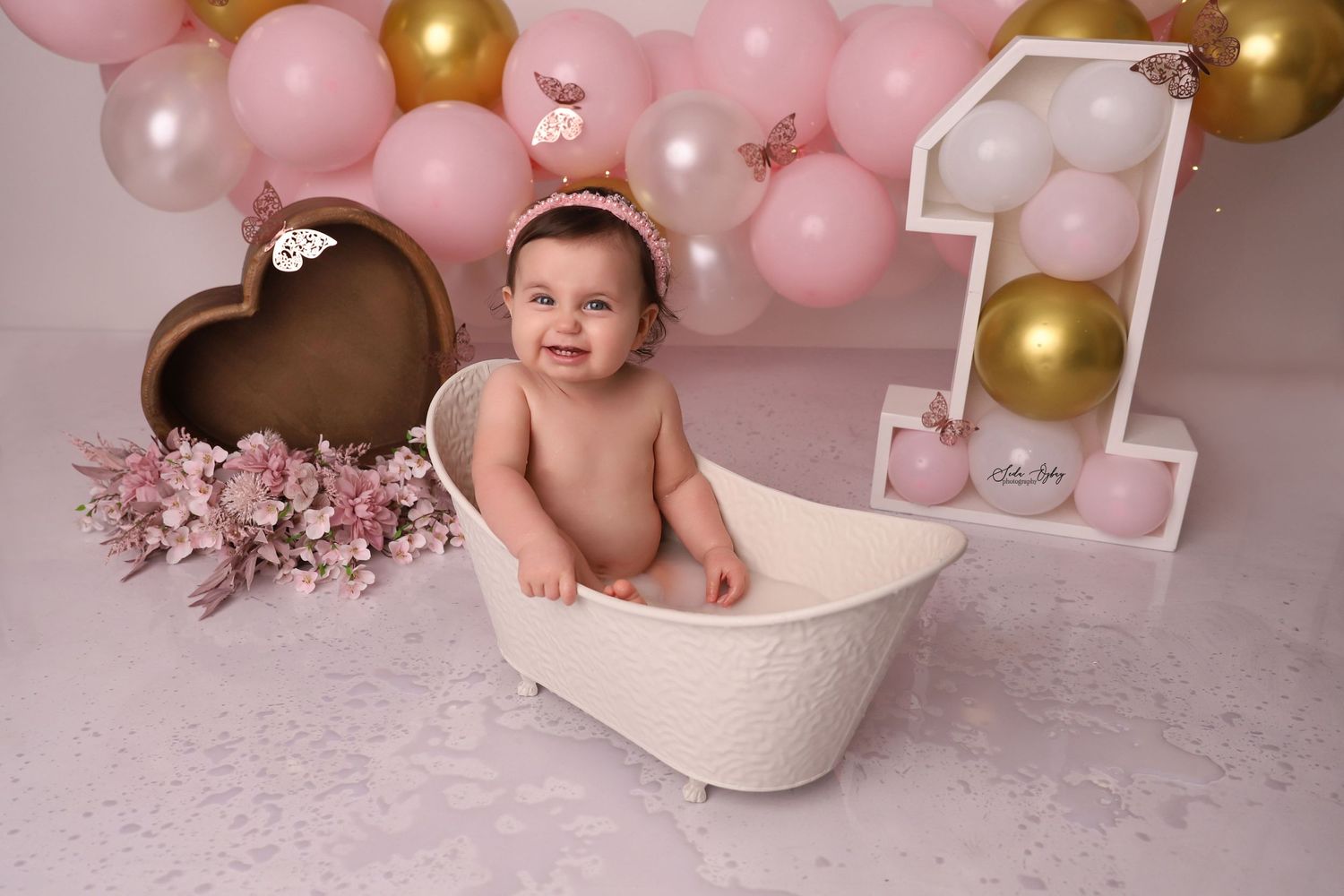 Baby's first birthday photoshoot with pink and gold balloon arch and decorative heart.