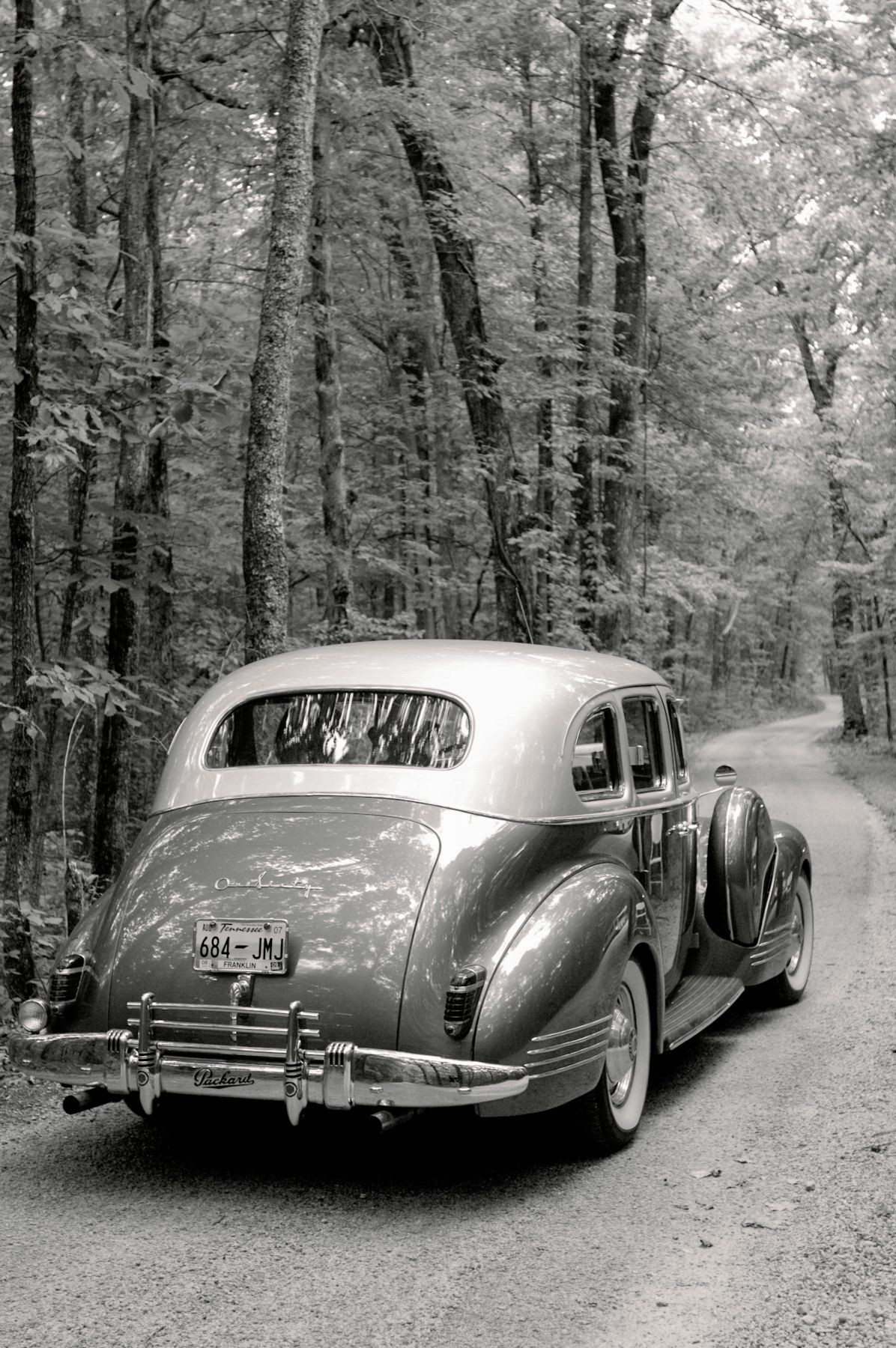 Classic vintage car parked on a wooded forest road in black and white photography.