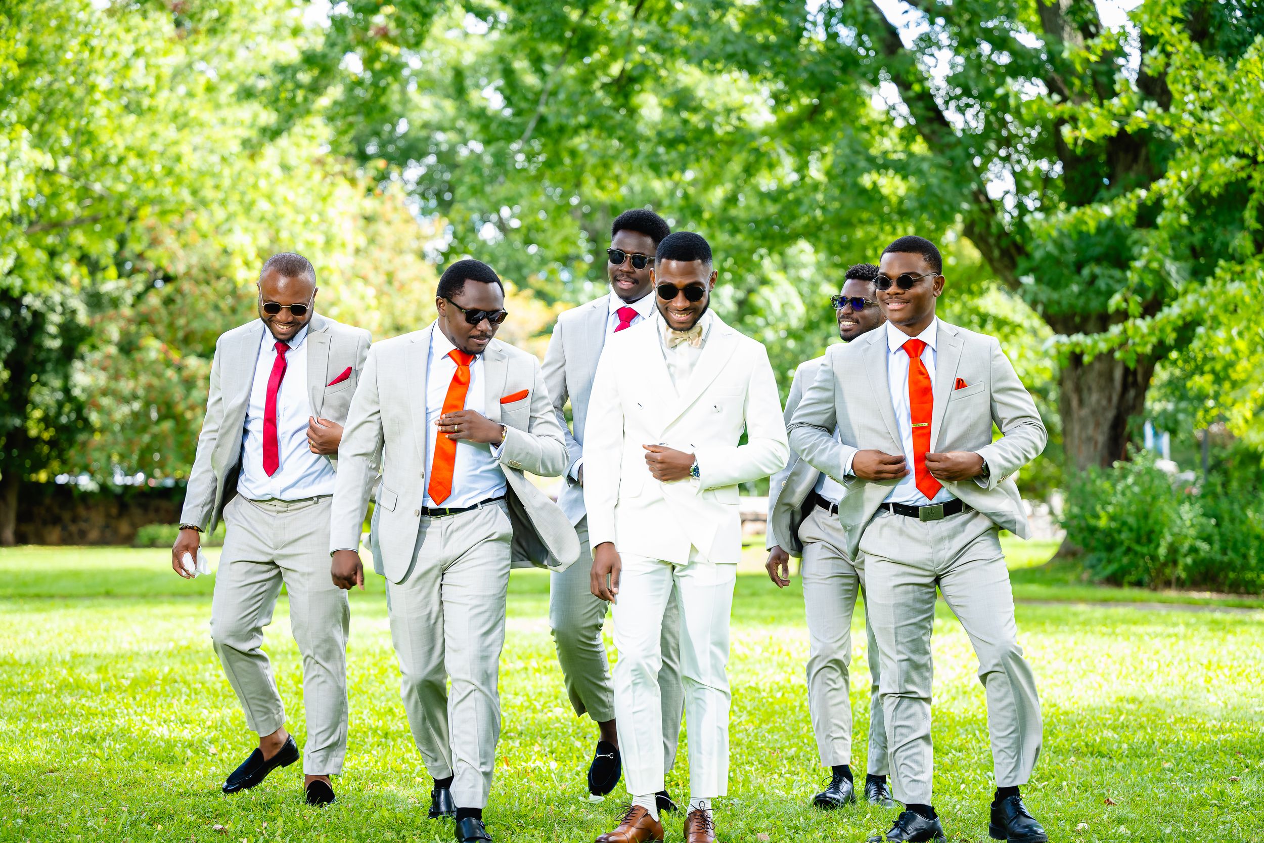 "Groupe de garçons d'honneur élégants marchant avec le marié dans un parc ensoleillé, capturé par Payo Studio lors d'un mariage."