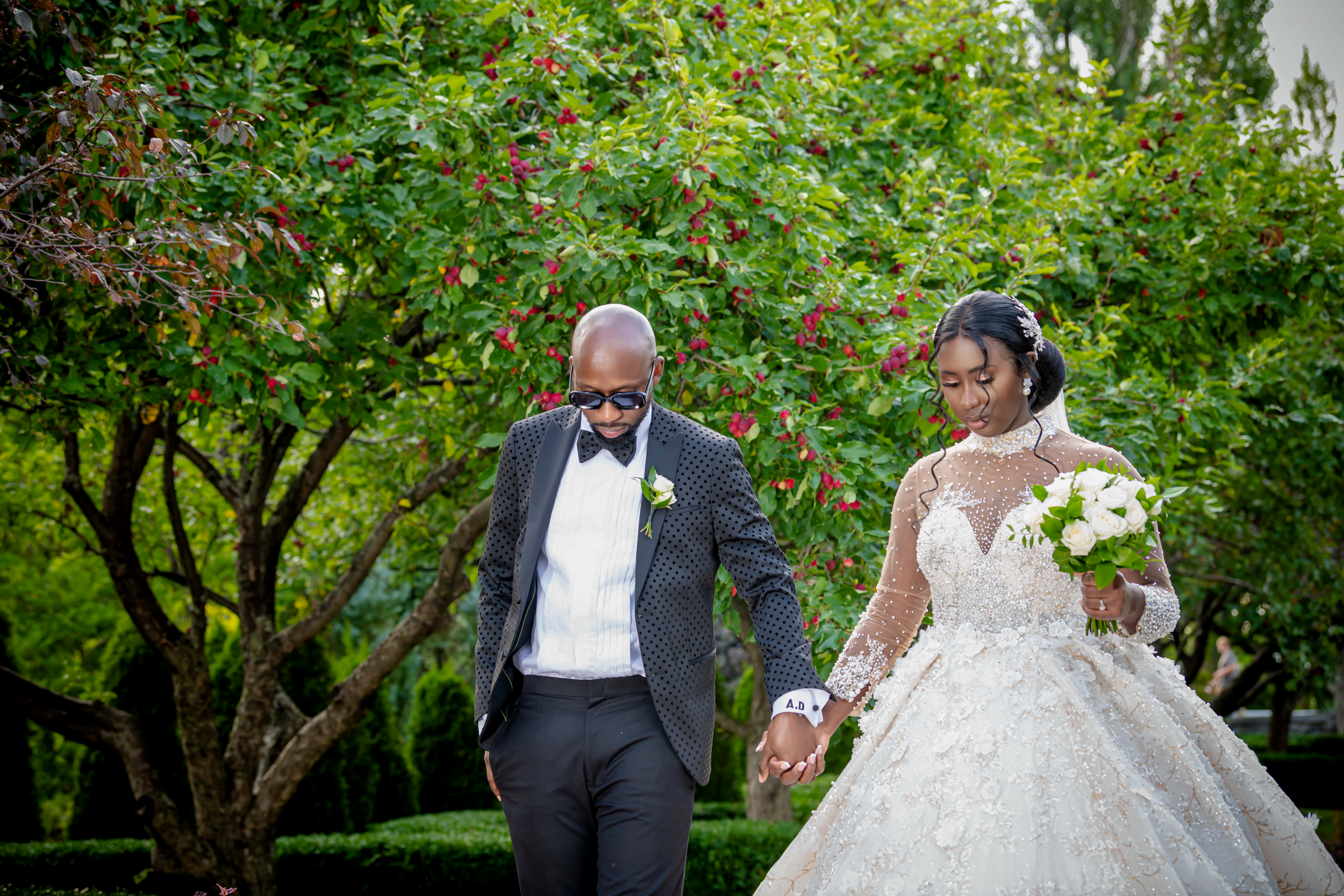 "Couple de beaux mariés marchant main dans la main dans un jardin verdoyant, capturé par Payo Studio lors d'un mariage élégant et féérique"