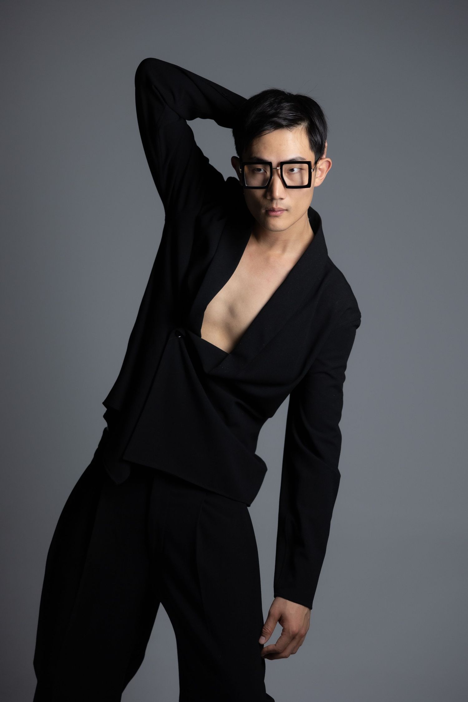 Fashion portrait of model in black blazer and glasses against grey background.