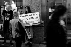 Street protesters holding sign that reads 'Unicorns are Vegan' in black and white.