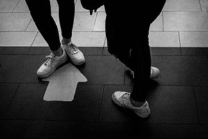 Black and white photo of feet in sneakers on tiled floor.