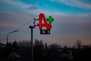 A red pharmacy cross sign illuminated against a dusky blue sky.