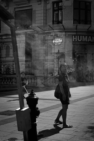 Black and white street scene showing pedestrians and shadows on a European sidewalk.