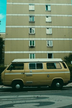 Vintage gold Volkswagen van parked in front of a beige apartment building with uniform windows.