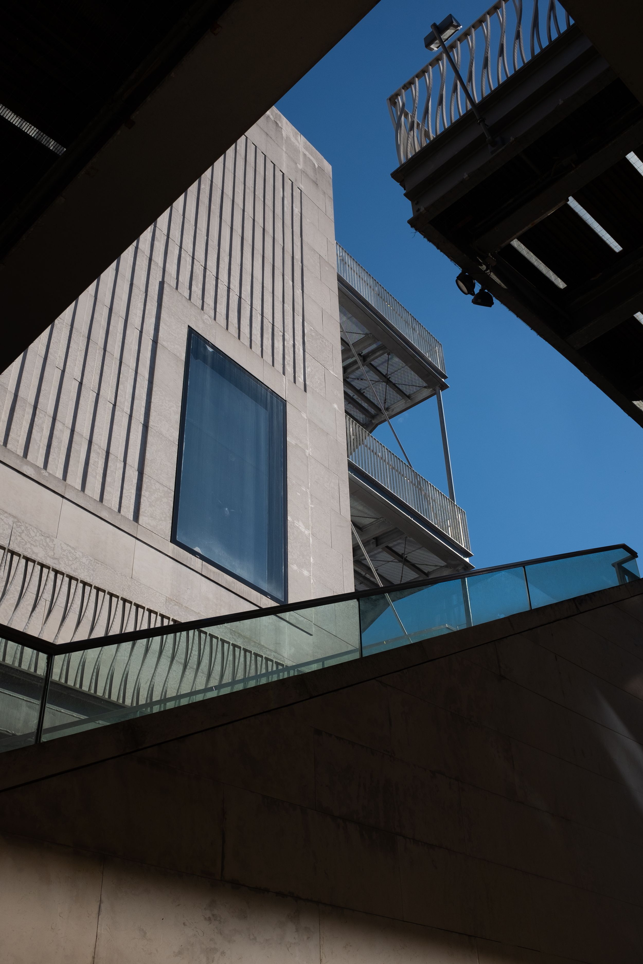 Modern brutalist architecture with concrete walls and glass panels against bright blue sky.