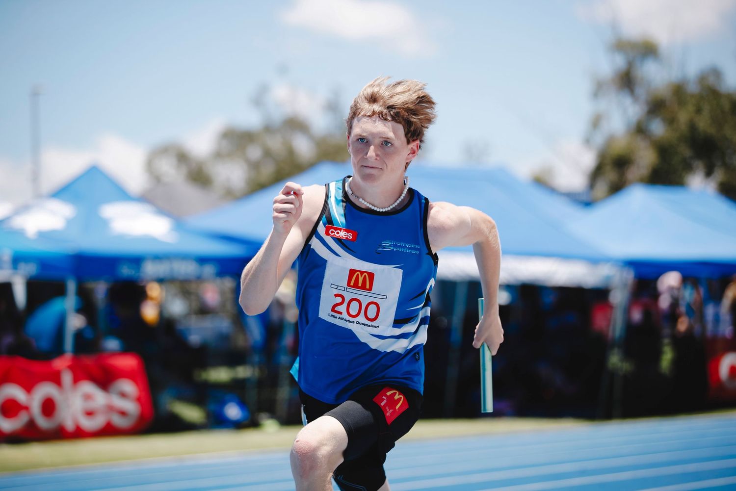 Track athlete in blue uniform sprinting during outdoor competition.