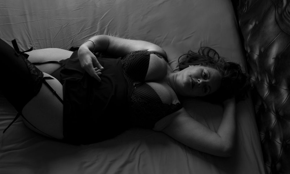 A black and white photo of voluptuous woman laying on a bed wearing black lingerie.