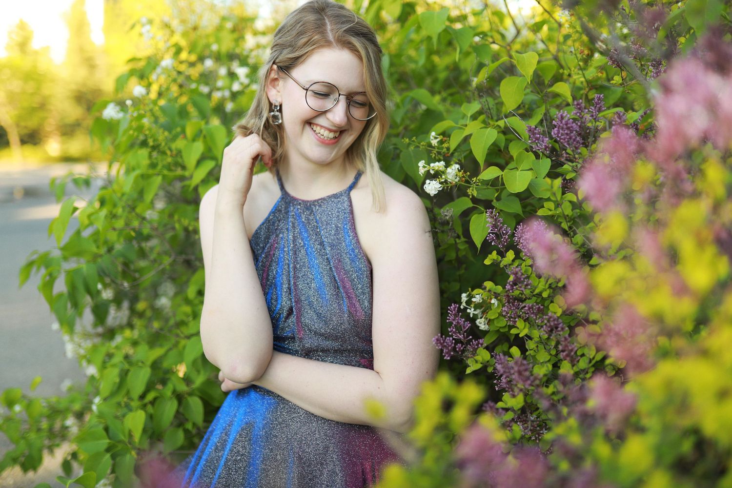 Someone in a blue dress stands smiling among blooming spring foliage and flowers in warm sunlight.