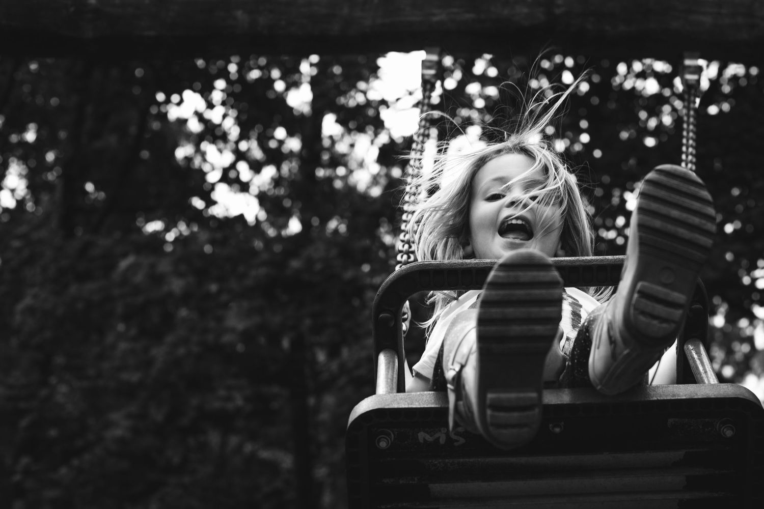 Black and white photo of joyful child swinging high on playground equipment.