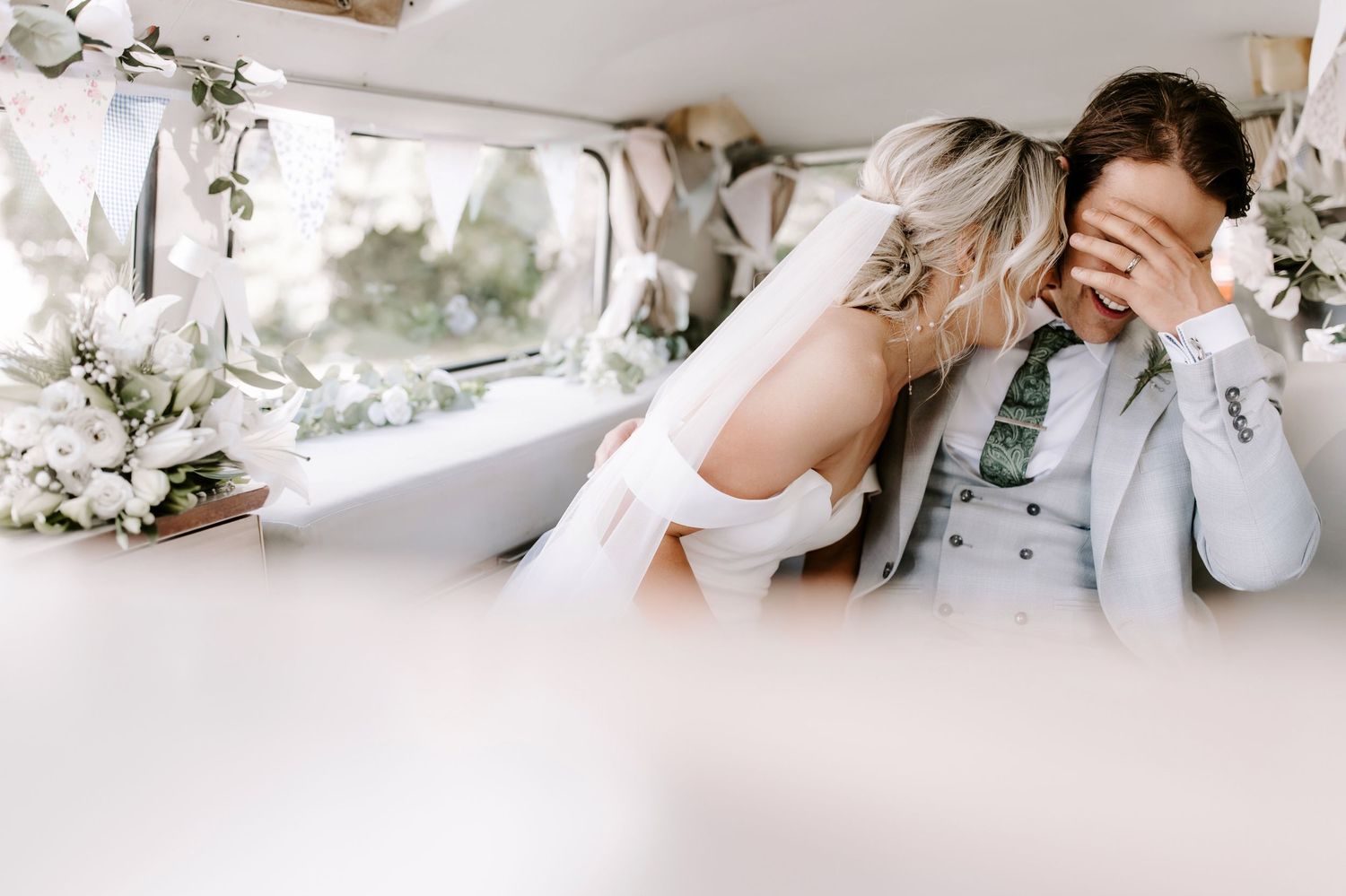 A romantic moment captured in the back of a vintage car decorated with white flowers for a wedding celebration.