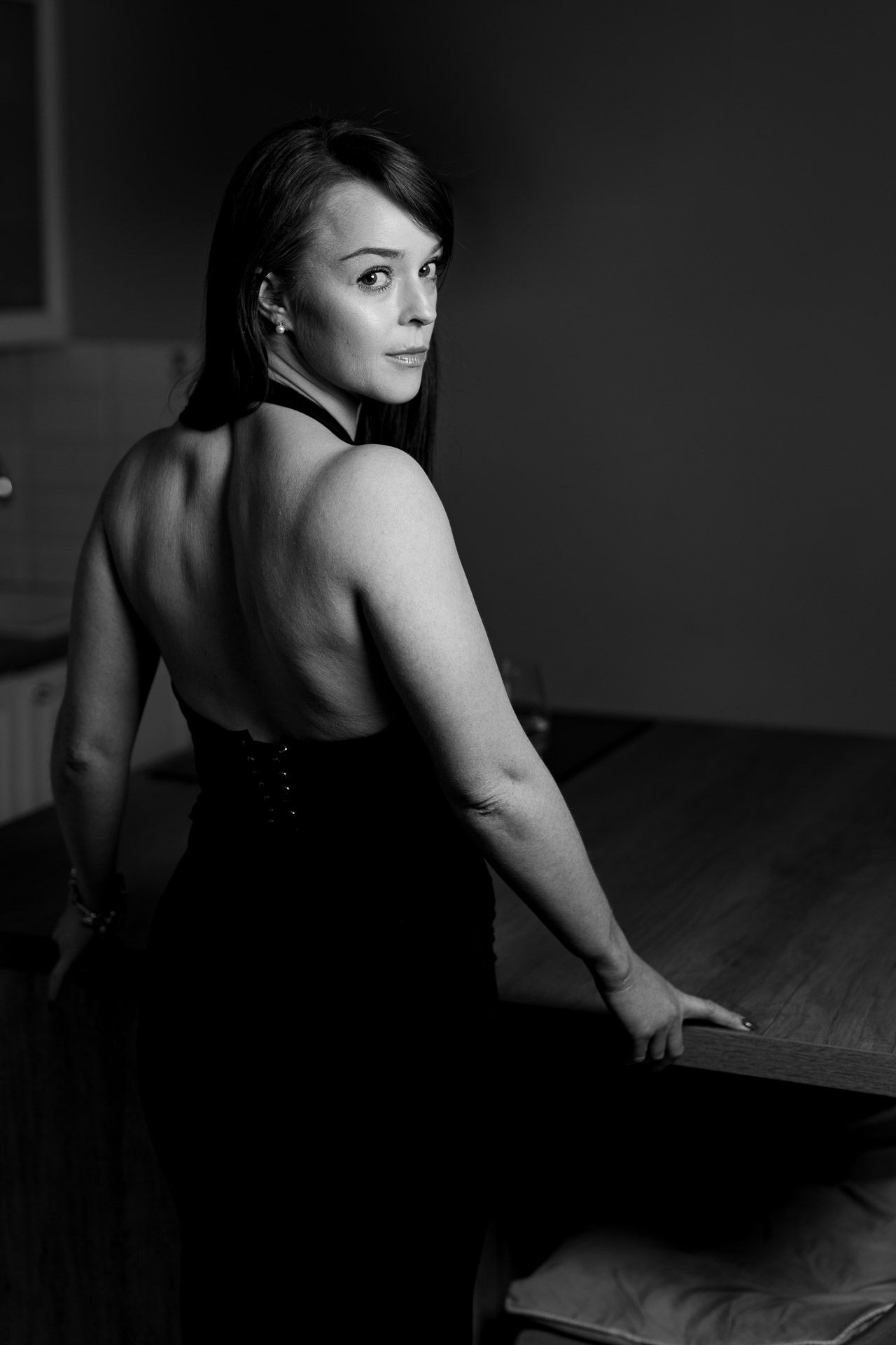 Dramatic monochrome photo of a woman in an elegant black dress posed against a dark background.
