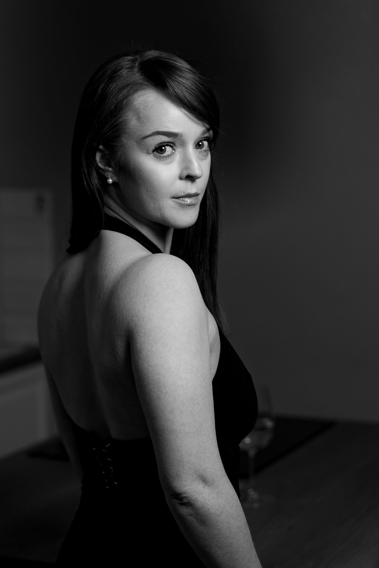Black and white portrait of a woman in a backless dress looking over her shoulder in dramatic lighting.
