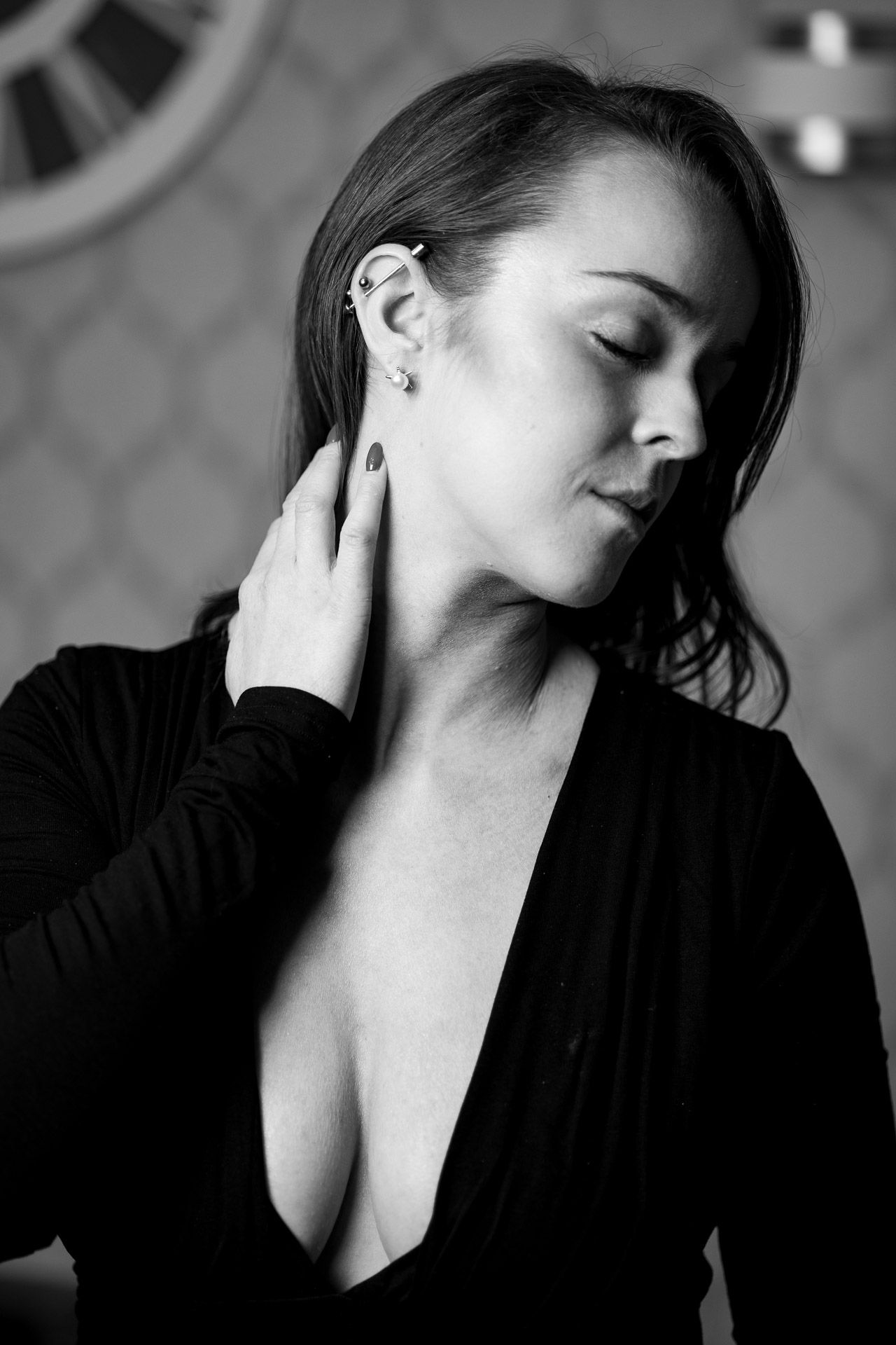 Artistic black and white portrait of woman in low-cut black top with eyes closed touching her neck.