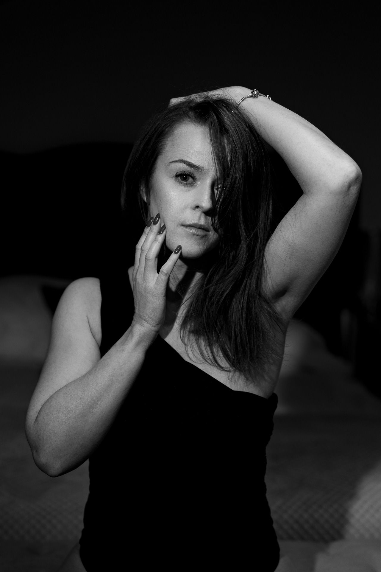 Black and white portrait of a woman in a dark top posing with dramatic lighting against a dark background.