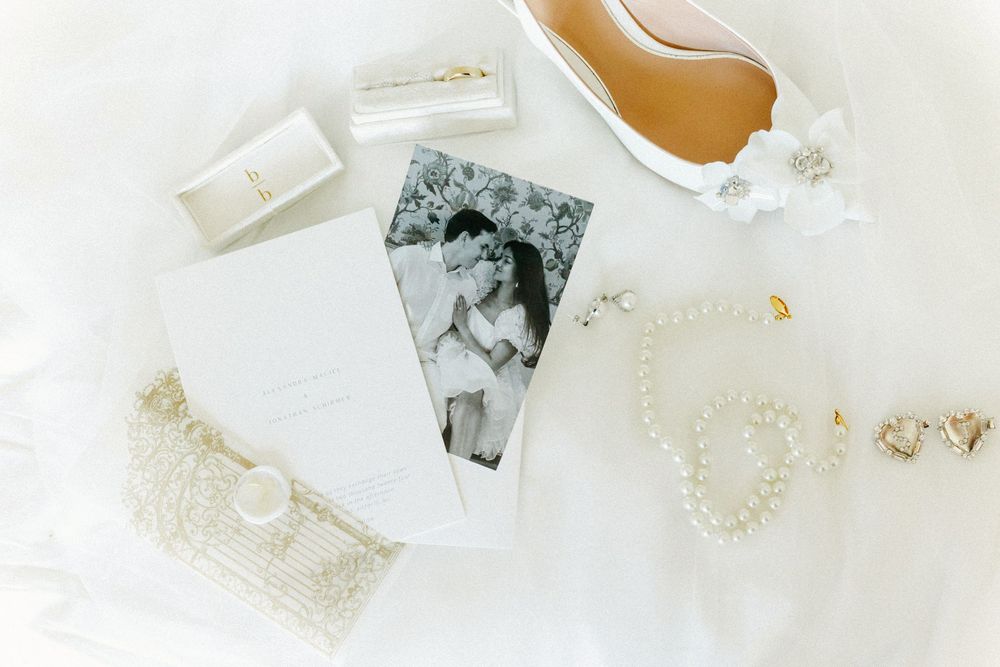 Wedding details including vintage photographs and pearls arranged on white surface.