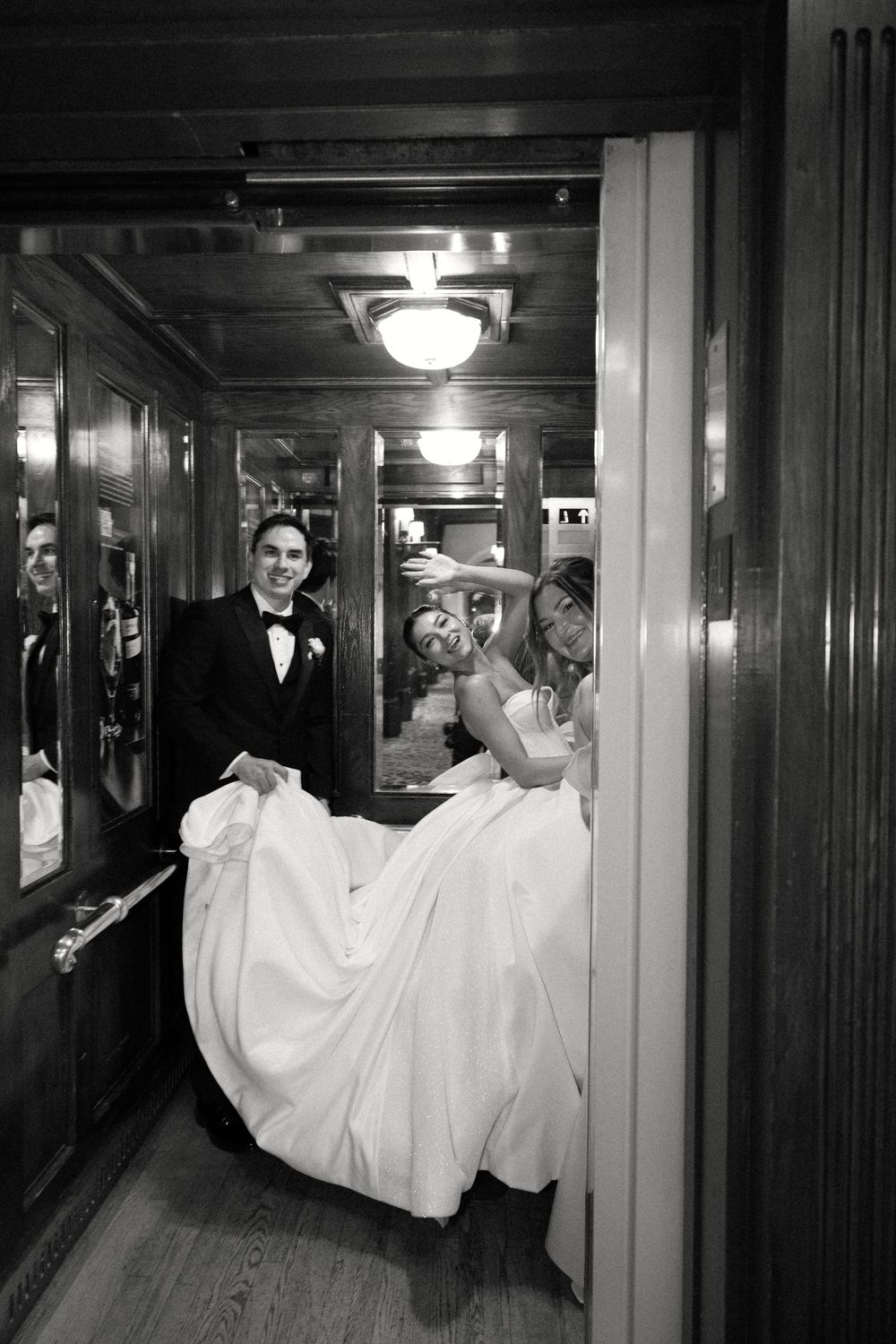 Black and white photo of newlyweds being carried through an elegant hotel hallway.