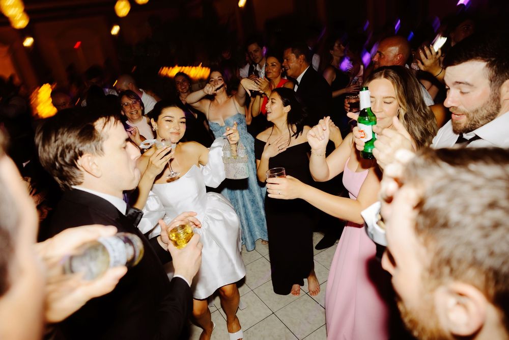Lively dance floor scene at wedding reception with guests dancing under colorful lights.