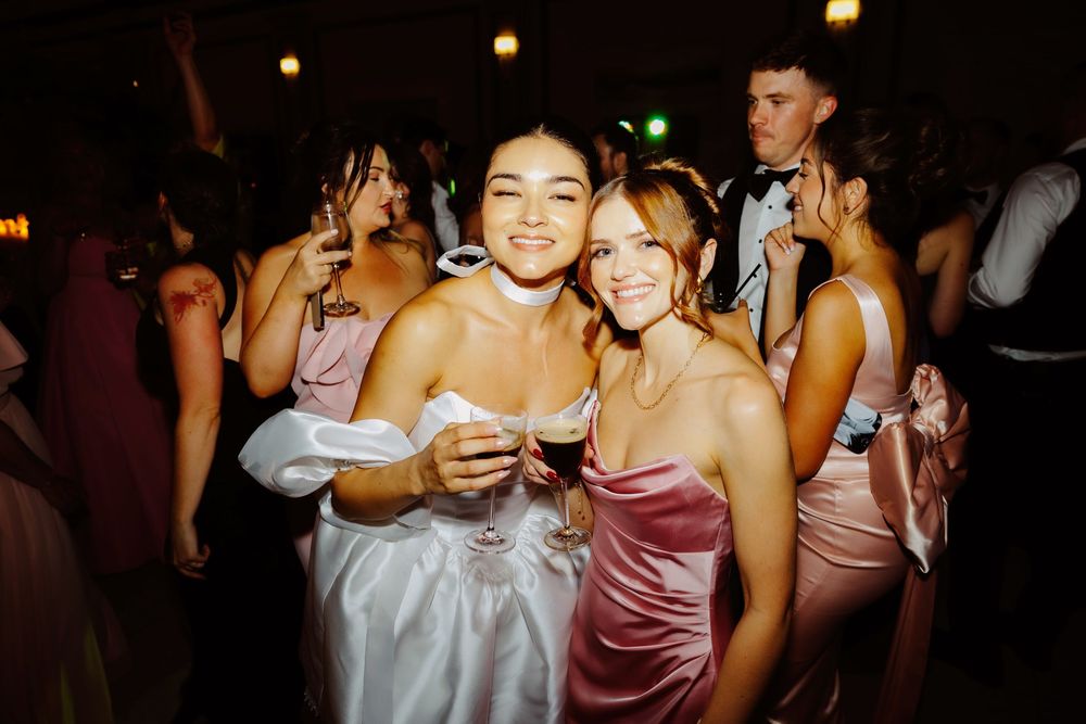 Wedding guests dance and celebrate at a lively reception party with warm lighting.