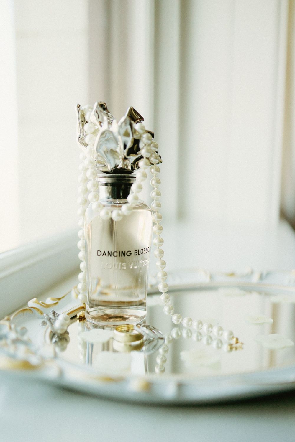 Perfume bottle labeled 'Dancing Blossom' with pearl necklace on mirrored tray.