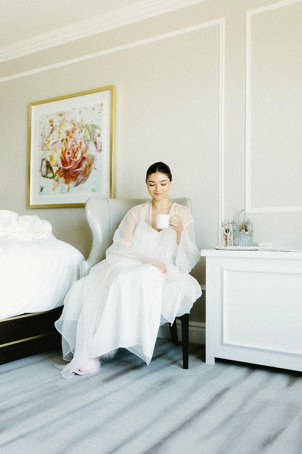 Bridal preparation scene in an elegant white room with artwork and furniture.