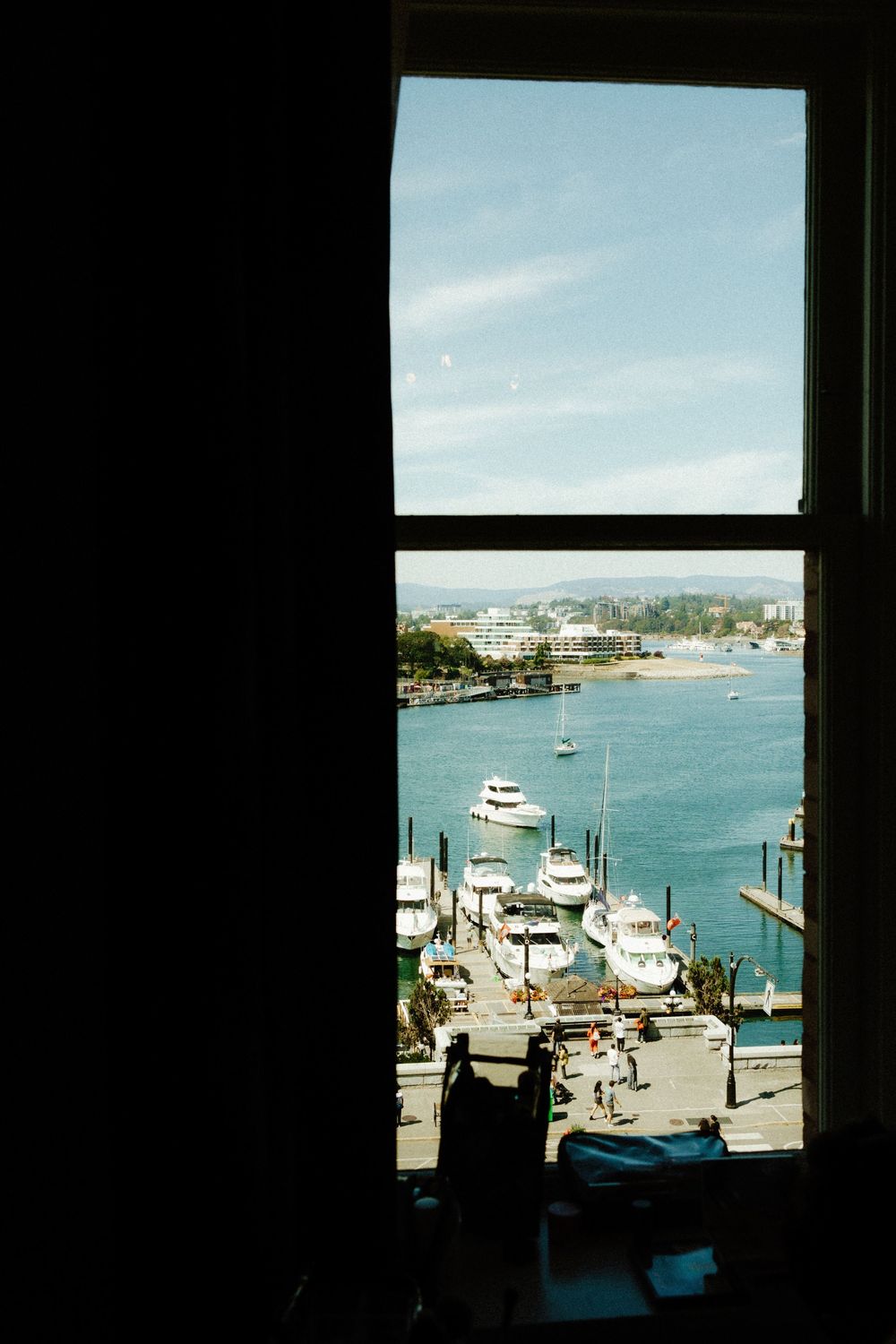 View of a marina with boats docked at the pier through a dark window frame.