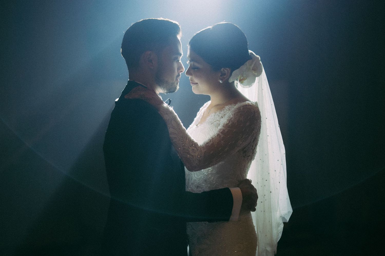 Romantic couple in wedding attire sharing an intimate moment under dramatic studio lighting.