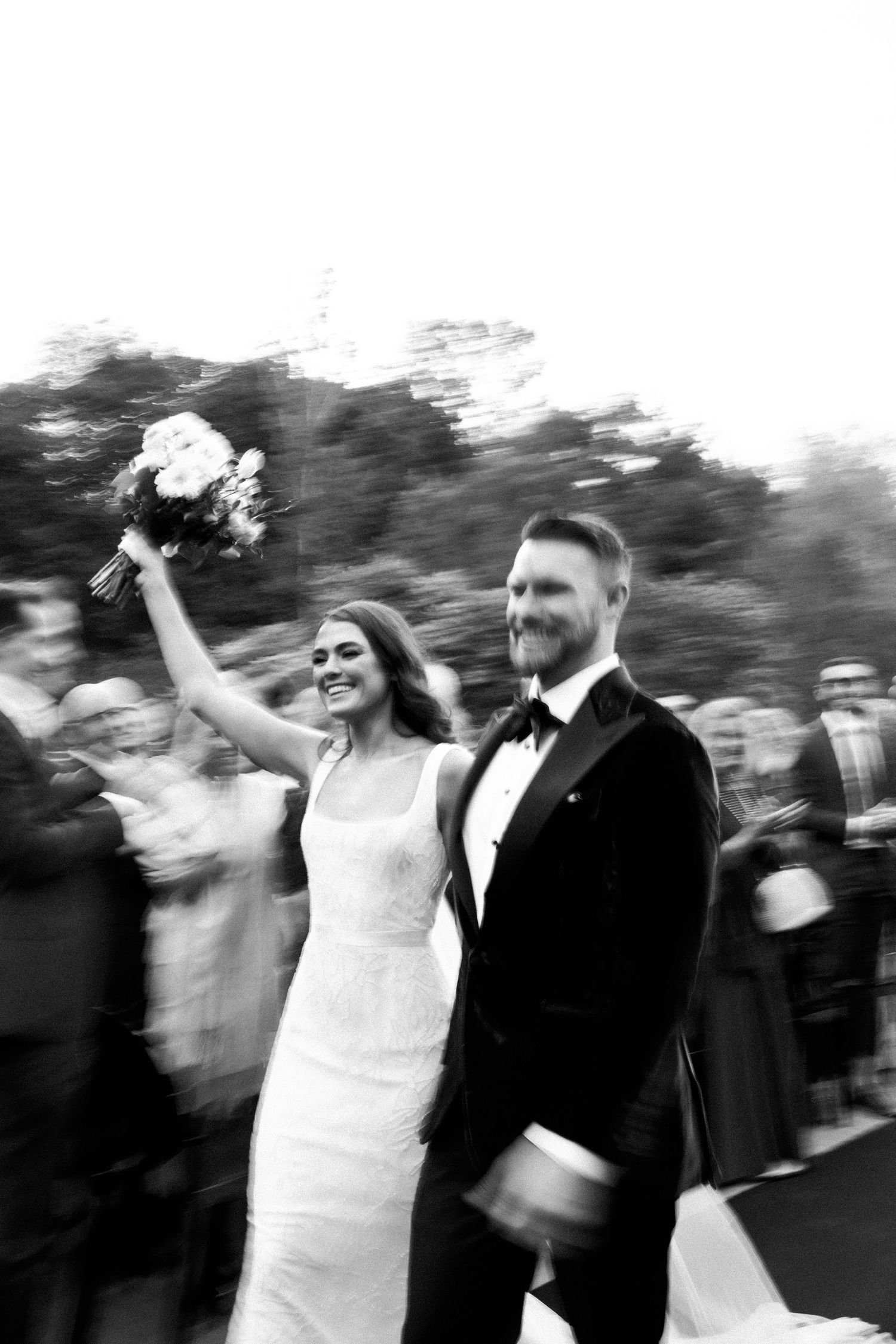 Black and white motion blur photograph of a joyful wedding celebration with couple walking together in formal attire.