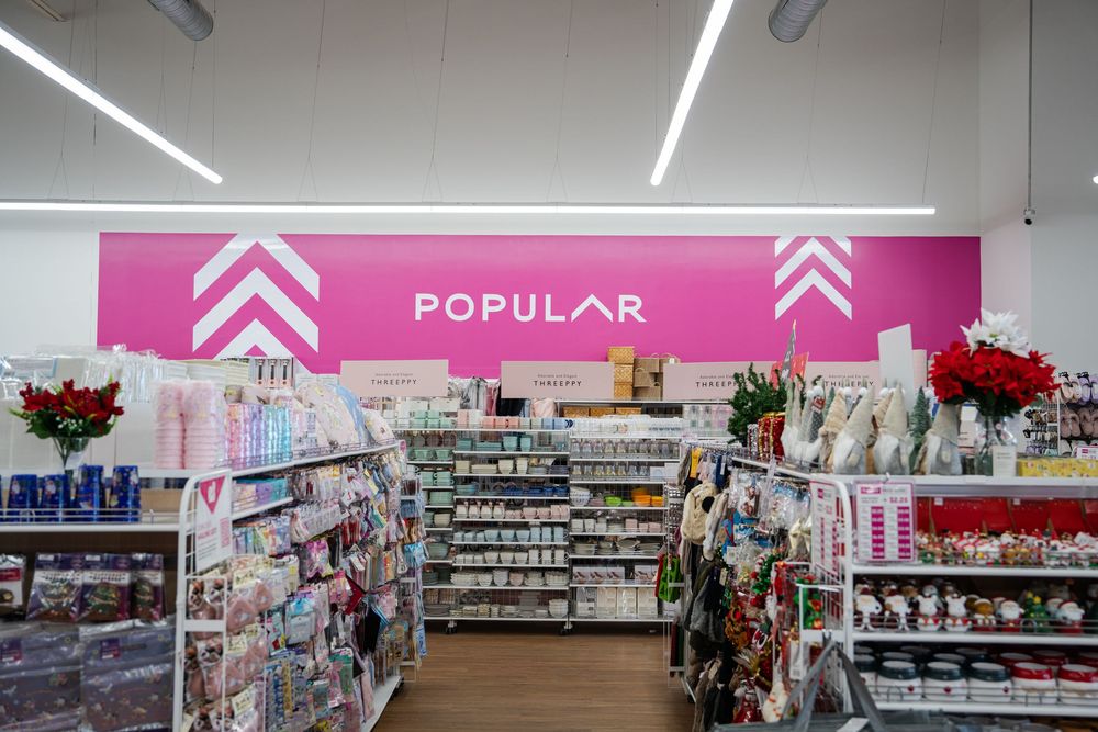 Interior view of a modern retail store with bright pink signage and white fluorescent lighting illuminating merchandise aisles.