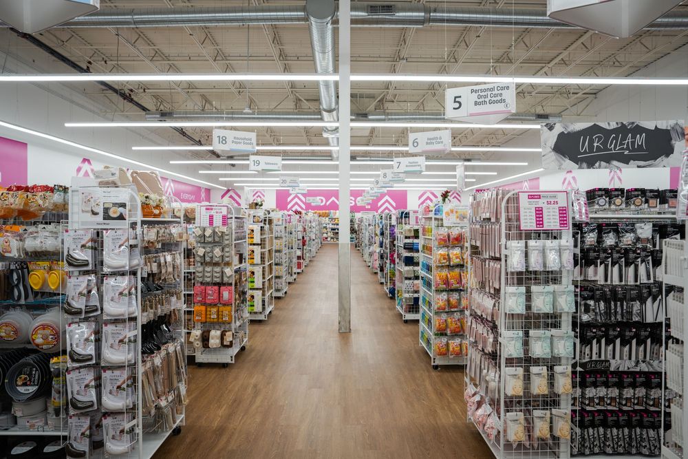 Long aisle view of a retail store interior with shelves of merchandise and bright fluorescent lighting overhead.