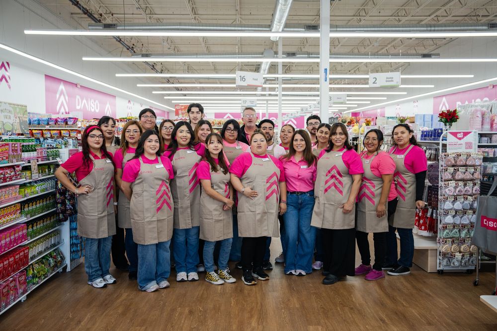 Retail store employees in matching uniforms pose for group photo in front of store shelves.