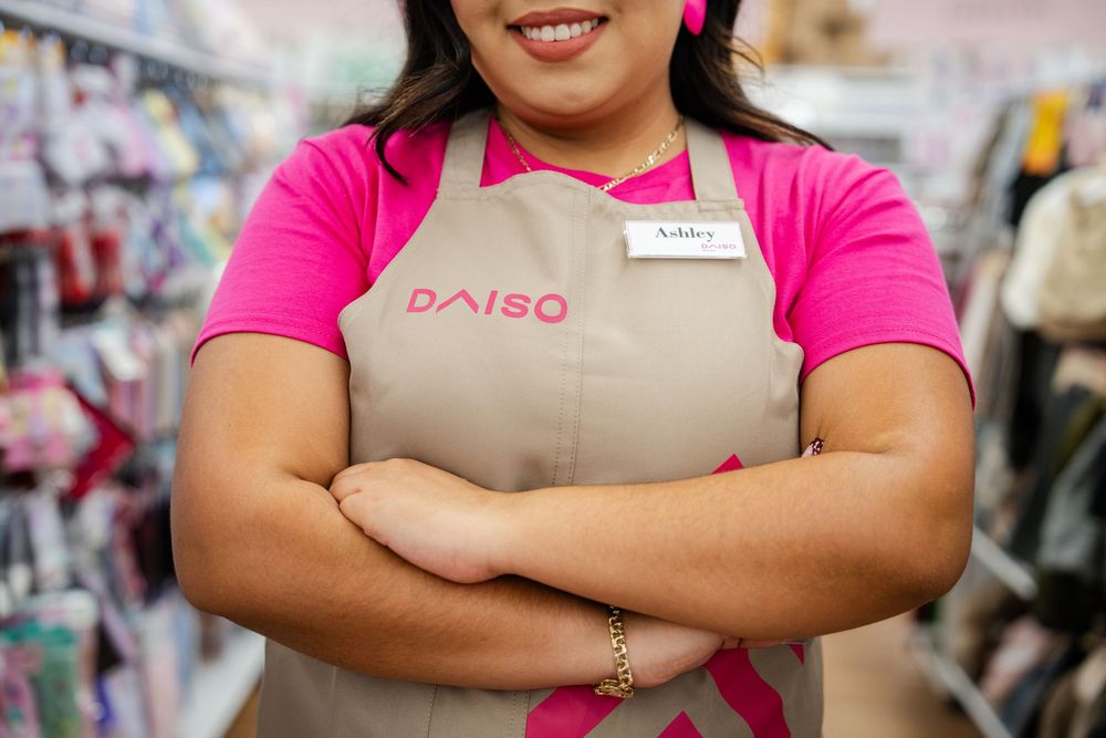 Retail workers in bright pink shirts and tan aprons stand together in a store aisle.