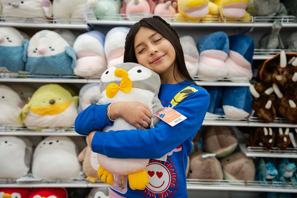 Plush toys and stuffed animals displayed on retail store shelves with soft pastel colors.