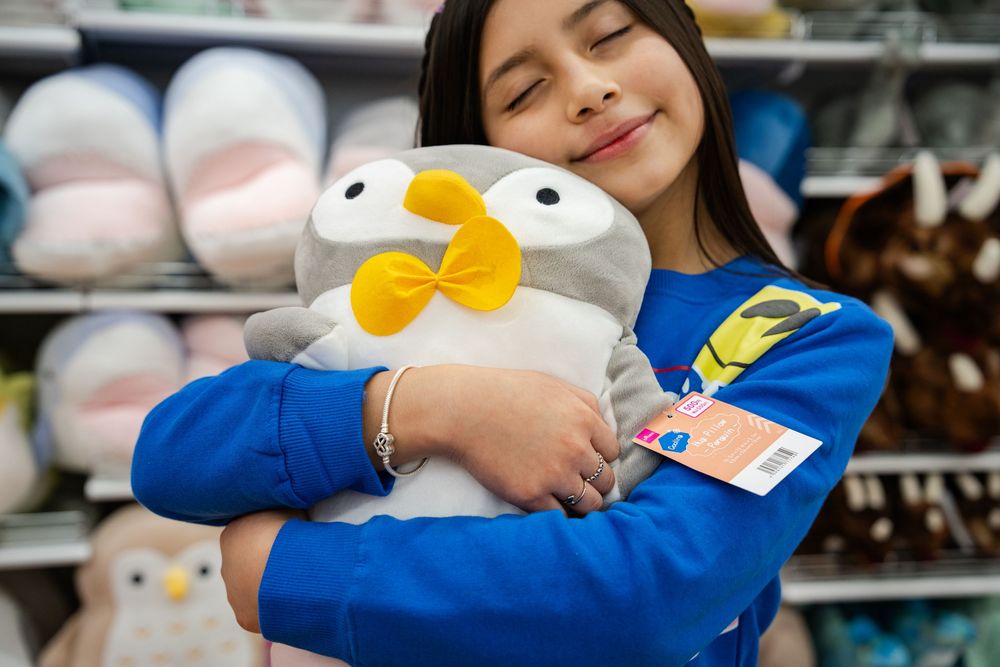 A person in a blue shirt holds a large plush Donald Duck toy while shopping in a store.