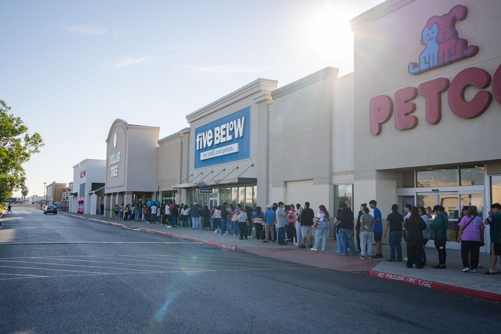 Long line of customers waiting outside shopping center stores during early morning hours.