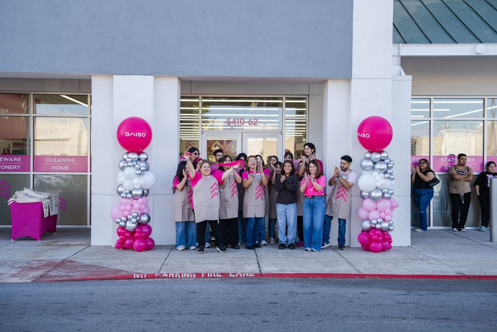 A panoramic view shows people gathered outside a modern building with pink balloon decorations along the exterior wall.