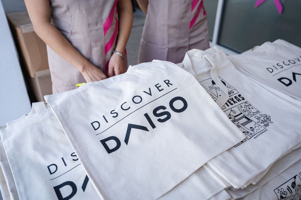 Hands unfolding and stacking white Discovery branded paper bags on a light surface.